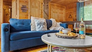 Um quarto aconchegante com um sofá azul, uma mesa redonda com petiscos e bebidas, e um letreiro escrito 'LIVE LAUGH LOVE'.
