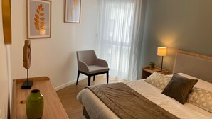 A hotel room with a bed, a chair, a nightstand with a lamp, and artwork on the walls. -  ZENAO Appart'hôtels Dijon (Dijon)