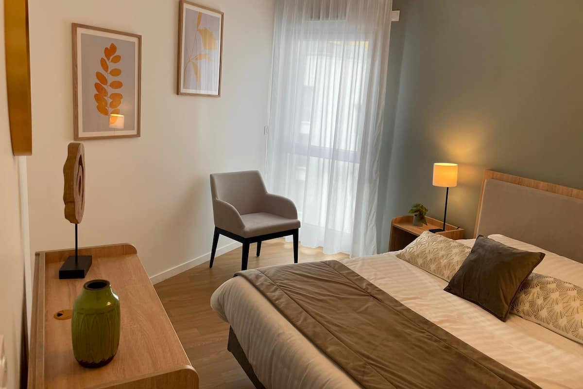 Une chambre d’hôtel avec un lit, une chaise, une table de chevet avec une lampe et des œuvres d’art accrochées aux murs.