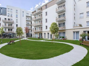 Un moderno edificio de apartamentos con varios balcones, un patio central con césped y bancos.