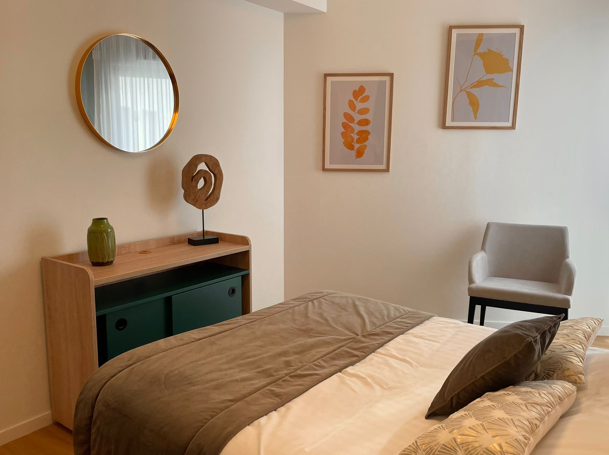 A bedroom with a bed, a dresser, a chair, and two framed artworks on the wall.