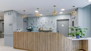 A reception area with a wooden reception desk, a wall-mounted plant, and a ceiling with recessed lighting. -  ZENAO Appart'hôtels Dijon (Dijon)