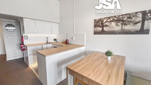 Een moderne keuken met witte kastjes, een houten aanrecht en een klein eiland. Op de muur hangt een schilderij van bomen en op de tafel staat een klein plantje.