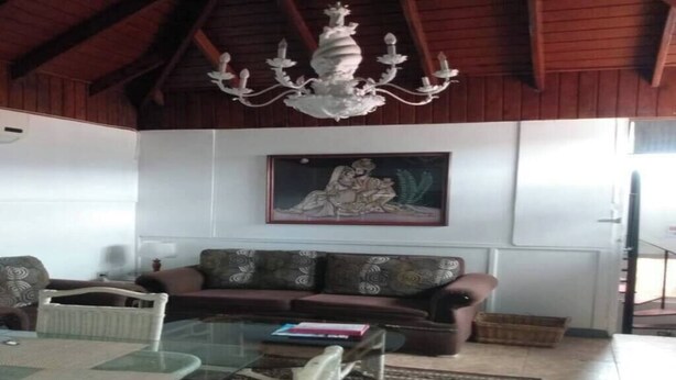 A living room with a glass coffee table, a brown sofa, and a chandelier. - Cozy 3 Apartment — Penthouse in the Heart of Ochi (Ocho Rios)