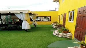 A courtyard with artificial grass, a covered seating area, and potted plants along a pathway. - Cozy 3 Apartment — Penthouse in the Heart of Ochi (Ocho Rios)