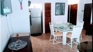 A dining area with a glass table and white chairs, a refrigerator, and a chalkboard with writing on the wall. - Cozy 3 Apartment — Penthouse in the Heart of Ochi (Ocho Rios)