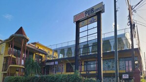 A building with a sign reading "Little PUB COMPLEX" and another sign for "Nash Supermarket." - Cozy 3 Apartment — Penthouse in the Heart of Ochi (Ocho Rios)
