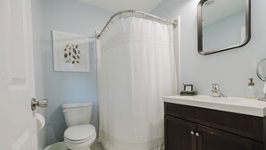 A bathroom with a white toilet, a white shower curtain, a dark wooden vanity, a white sink, and a framed picture on the wall.