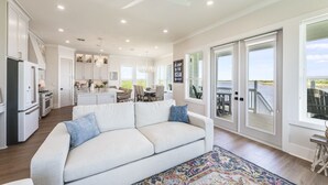 Een ruime woonkamer met een witte bank, een keuken en een balkon met uitzicht op de oceaan.