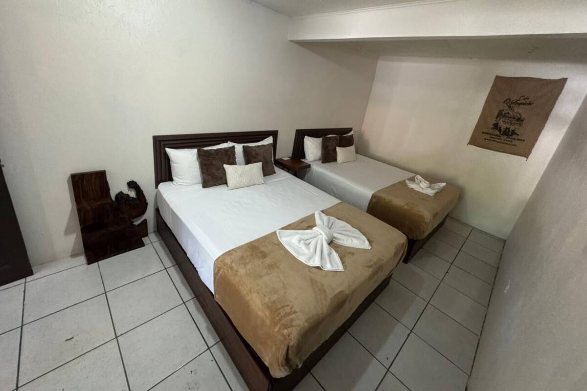 Une chambre d’hôtel avec deux lits, une tête de lit en bois, une petite table et un panneau fixé au mur.