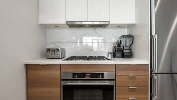 A modern kitchen with white cabinets, a built-in oven, a stovetop, a toaster, and a refrigerator.