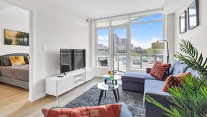 Una sala de estar moderna con un sofá, un televisor, una mesa de centro y un balcón con vistas a la ciudad.