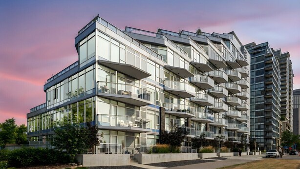 Un moderno edificio residencial de varios pisos con balcones, ventanas grandes y un patio ajardinado.