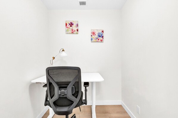 A small office space with a white desk, a black office chair, and two floral paintings on the wall.