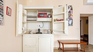 Cozinha compacta com micro-ondas, chaleira e pequeno armário.