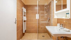Uma casa de banho moderna com cabine de duche em vidro, uma pia branca e um porta-toalhas.
