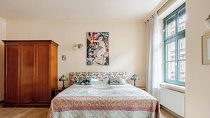 Quarto com cama grande, guarda-roupa de madeira, janela com cortinas e um quadro na parede.