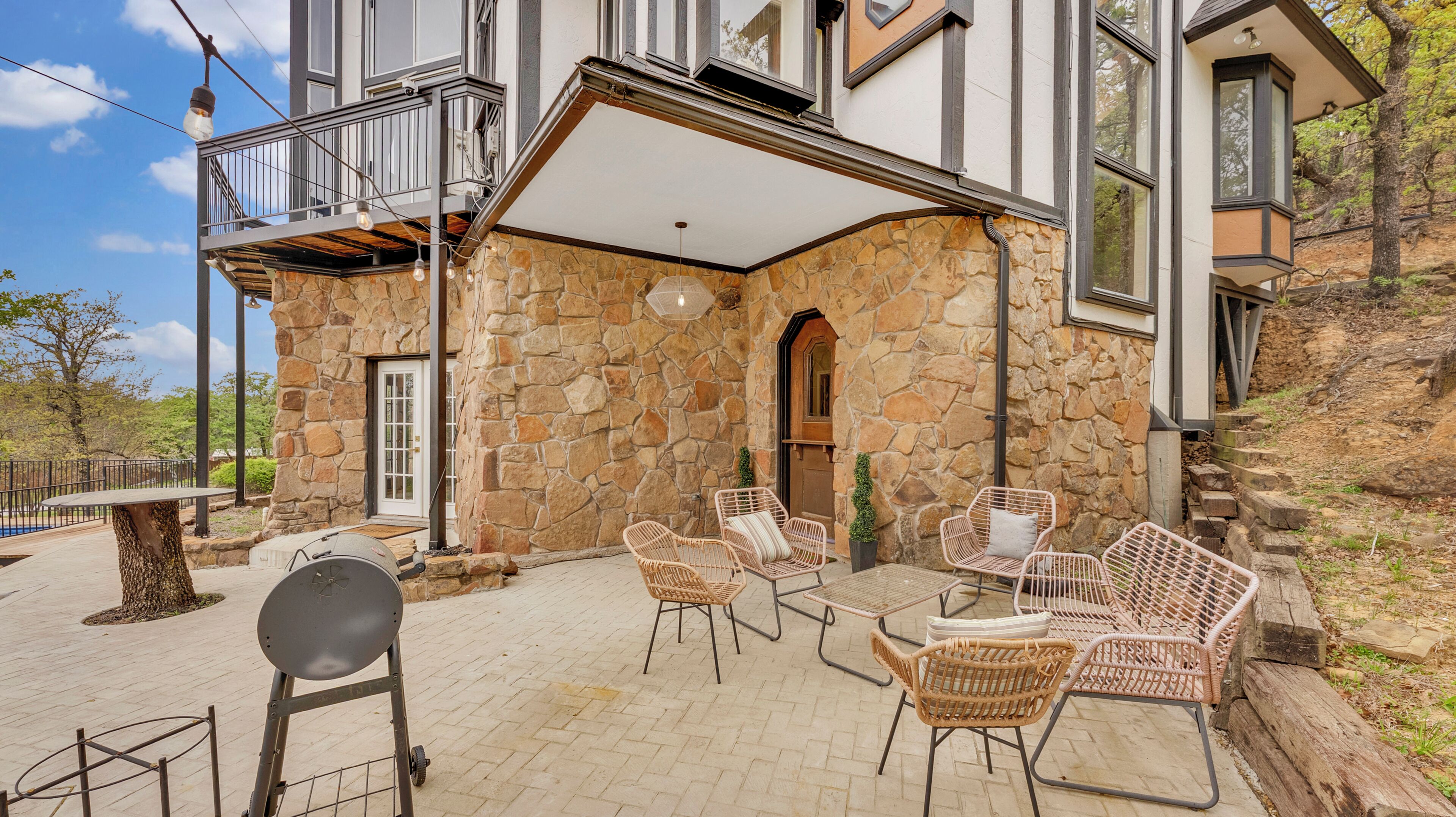 A stone building with a balcony, wicker chairs, and a barbecue grill.