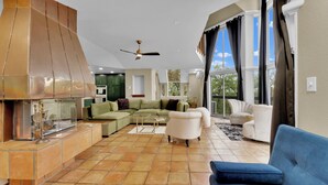 A spacious living area with a sectional sofa, a white armchair, a blue sofa, a fireplace, and a ceiling fan. - Highest House in All of Fort Worth - Luxury Family Getaway with Stunning Views (Joshua)