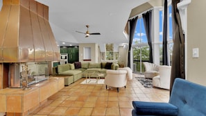 Amplia sala de estar con un sofá modular, un sillón blanco, un sofá azul, una chimenea y un ventilador de techo.