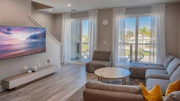 Een moderne woonkamer met een flatscreen televisie, een zithoek, een salontafel en een trap naar een balkon.