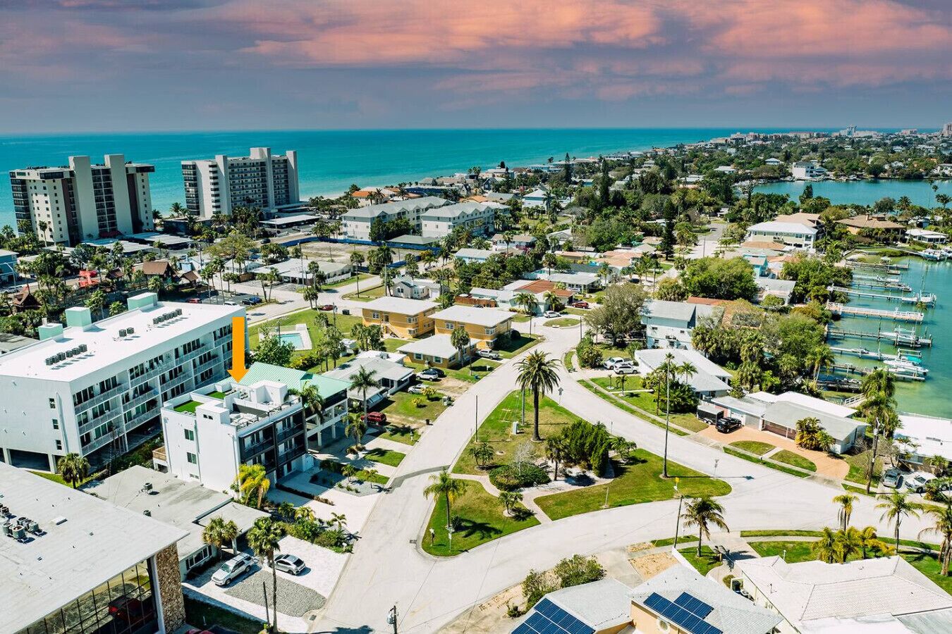 Vista aérea de un pueblo costero con un puerto deportivo, edificios residenciales y un hotel destacado con un diseño moderno.