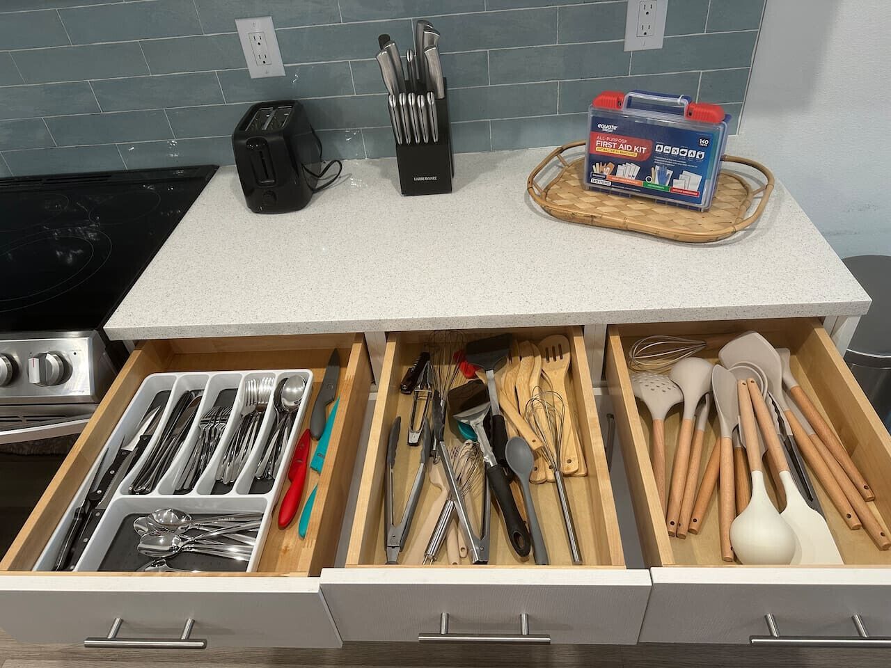 A kitchen drawer with utensils, a toaster, and a first aid kit on the countertop.