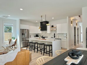 Una cocina moderna con armarios blancos, un refrigerador de acero inoxidable y una isla central con taburetes de bar.