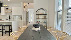 Une cuisine moderne avec des meubles blancs, un plan de travail en marbre et une table à manger en bois, accompagnée de chaises.