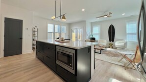 Une cuisine moderne dotée d’un îlot central, d’appareils électroménagers intégrés et de luminaires suspendus.