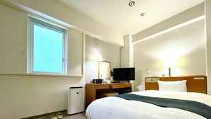 Ett hotellrum med en stor säng, ett skrivbord med en tv, en lampa och en telefon.
