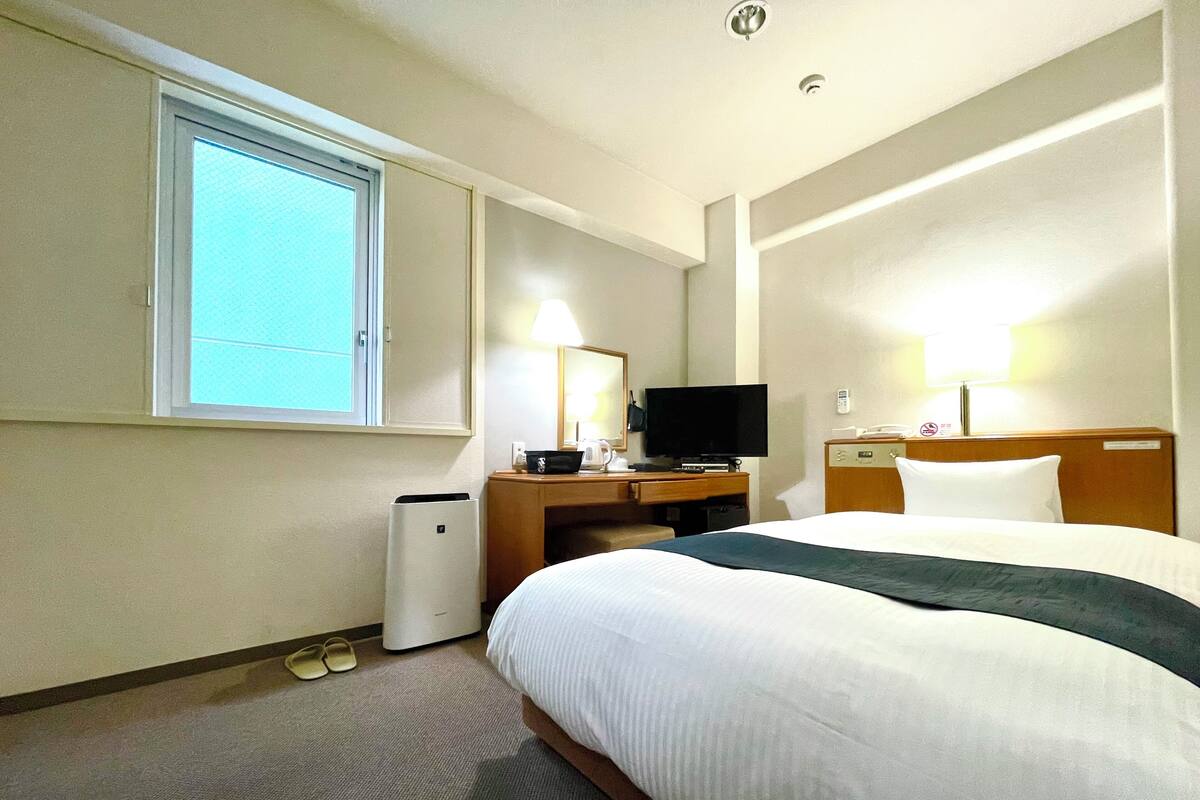 Ein Hotelzimmer mit einem großen Bett, einem Schreibtisch mit Fernseher, einer Lampe und einem Telefon.