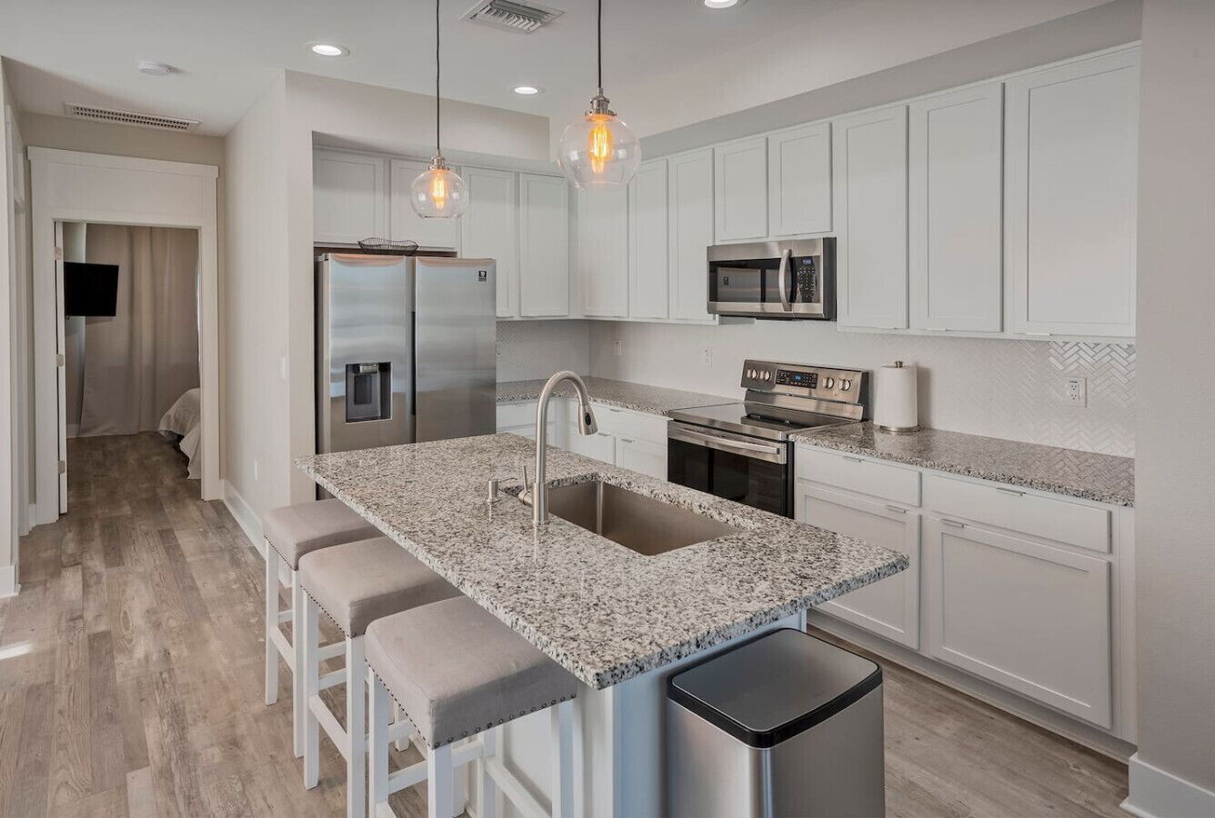 A modern kitchen with white cabinets, granite countertops, stainless steel appliances, and pendant lighting.
