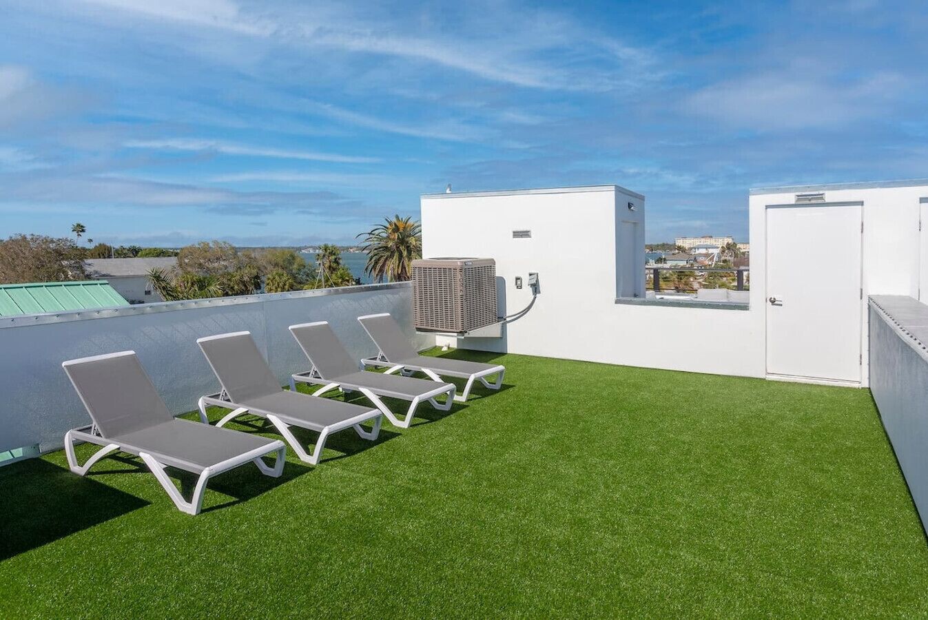 Terraza en la azotea con césped artificial, sillones blancos y un equipo de aire acondicionado.