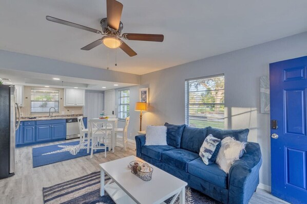 A modern living room with a blue sofa, a white coffee table, and a ceiling fan.