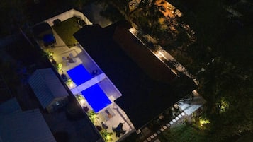 An aerial view of a residential property with a swimming pool, a covered patio, and a well-lit garden area.