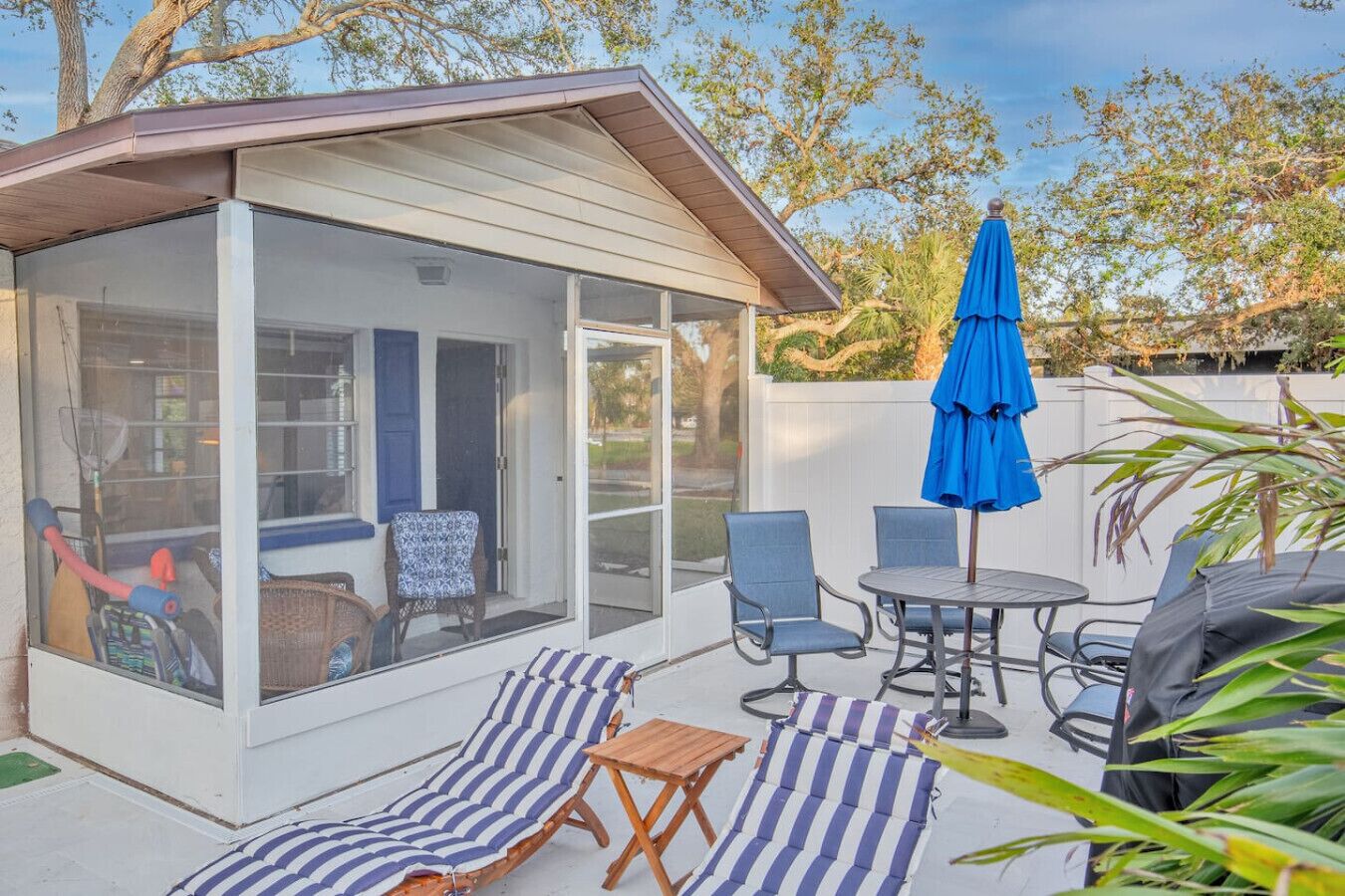 A covered patio with a glass enclosure, outdoor seating, and a blue umbrella.