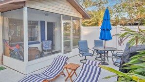 Eine überdachte Terrasse mit Glasveranda, Sitzgelegenheiten im Freien und einem blauen Sonnenschirm.