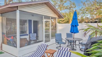 A covered patio with a glass enclosure, outdoor seating, and a blue umbrella.
