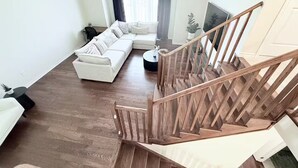 Un salon avec un escalier en bois, un canapé d’angle et un téléviseur fixé au mur.
