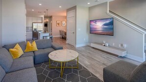 Ein modernes Wohnzimmer mit einem grauen Sofa, gelben Kissen, einem Marmor-Couchtisch und einem flachbildfernseher, der an der Wand befestigt ist.