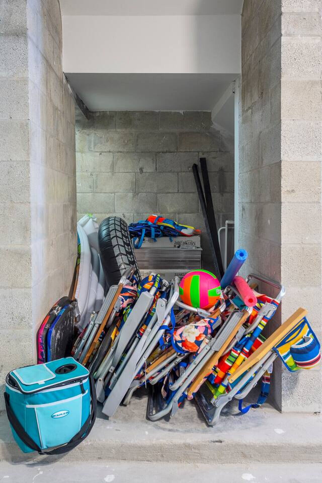 A storage area with various sports equipment, including skis, a volleyball, and a blue suitcase.
