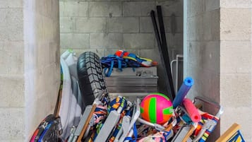 A storage area with various sports equipment, including skis, a volleyball, and a blue suitcase.