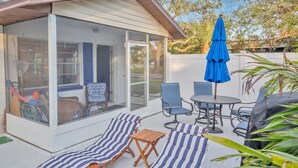 Eine überdachte Terrasse mit Glasveranda, Sitzgelegenheiten im Freien und einem blauen Sonnenschirm.