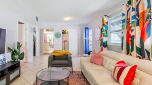 A living room with a sofa, a round coffee table, a grey armchair, and a TV on a stand. - Tropical Paradise-4/4 (Largo)
