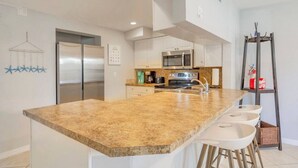 A modern kitchen with a large island, stainless steel appliances, and a hanging rack. - Tropical Paradise-4/4 (Largo)