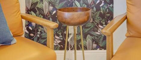 Une pièce avec deux fauteuils en cuir, un bol en bois posé sur un petit tabouret, et un mur orné d’un motif floral et d’un néon qui indique : « Ici, c’est notre havre de paix. »