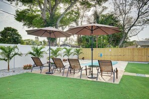 Een achtertuin met een zwembad, vier ligstoelen en twee parasols.