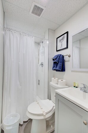 Een badkamer met een douche, toilet, wastafel en een ingelijst kunstwerk aan de muur.