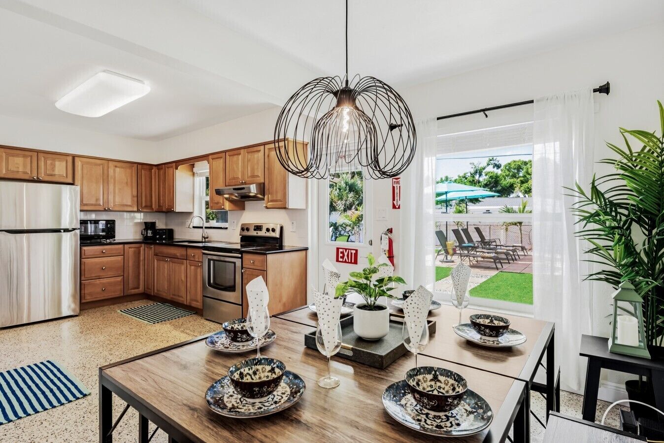 A modern kitchen with wooden cabinets, stainless steel appliances, and a dining area with a table set for four.